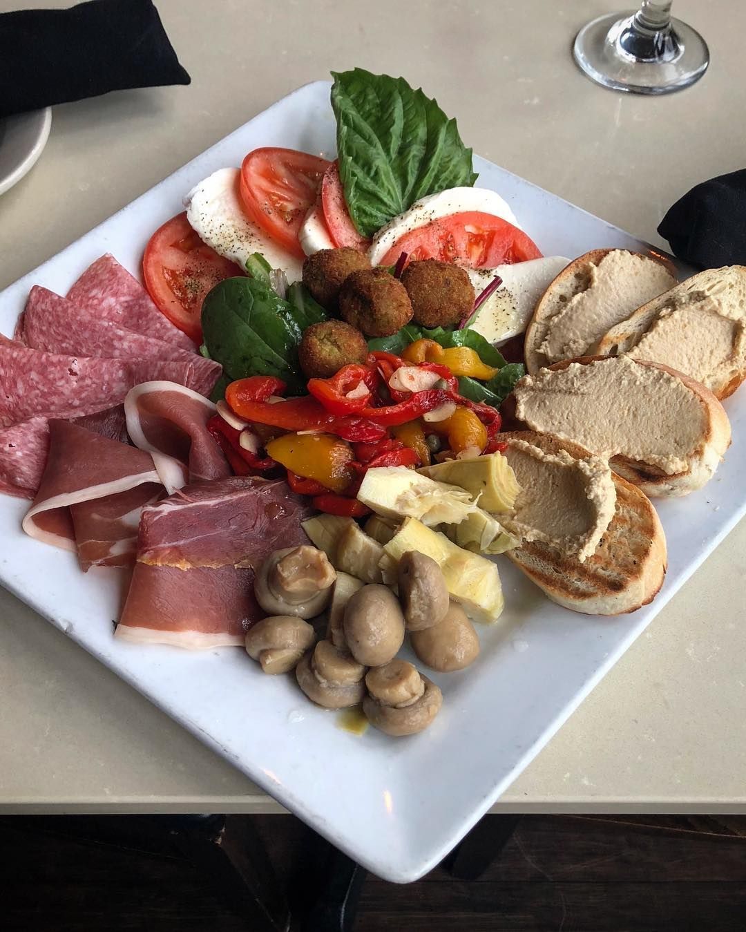 A close up of a plate of antipasto platter with olives and bruschetta and carved meats