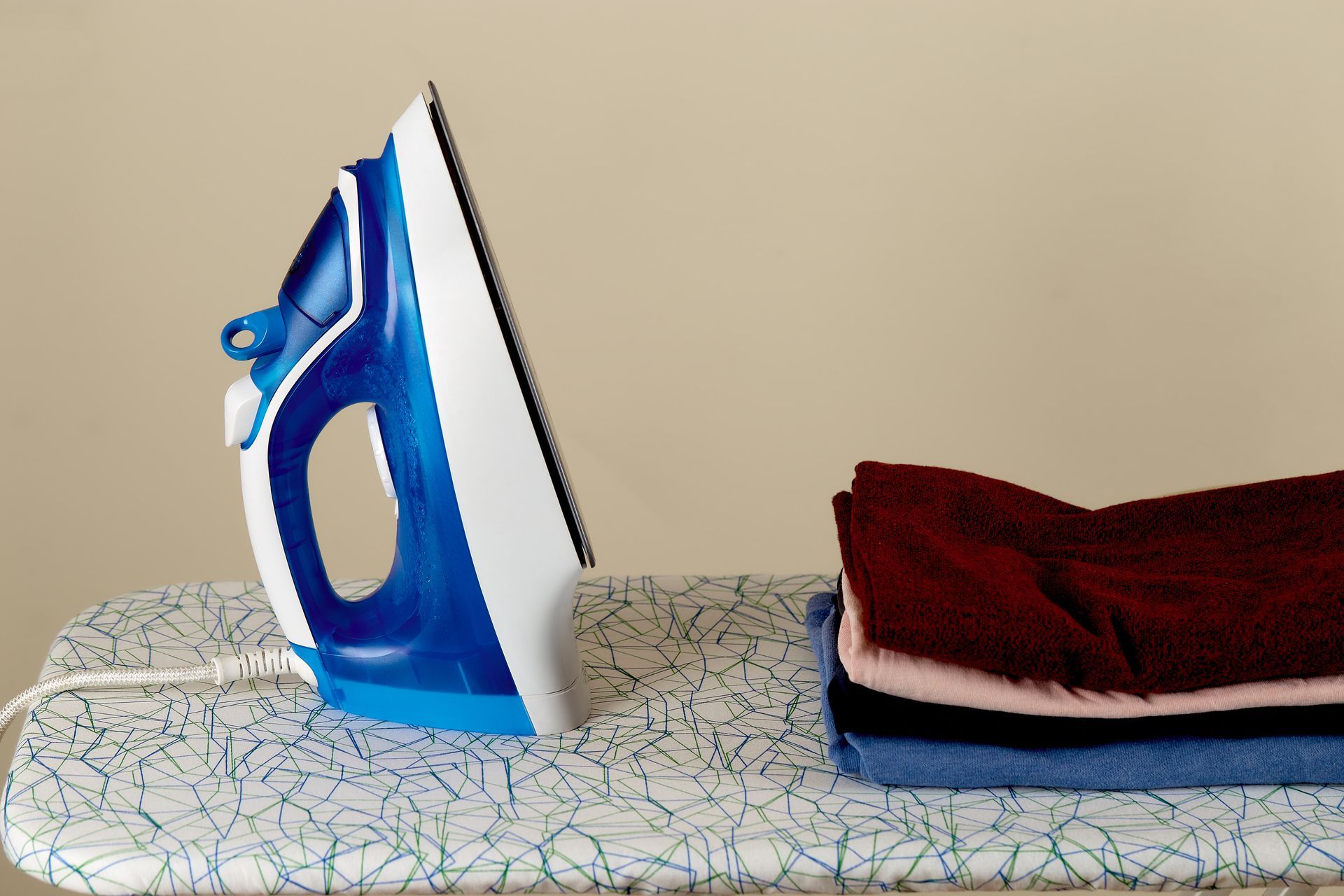 A blue and white iron is sitting on an ironing board next to a pile of clothes.