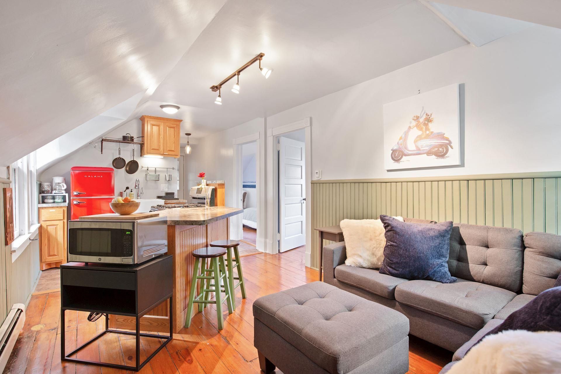 A living room with a couch and ottoman and a kitchen in the background.