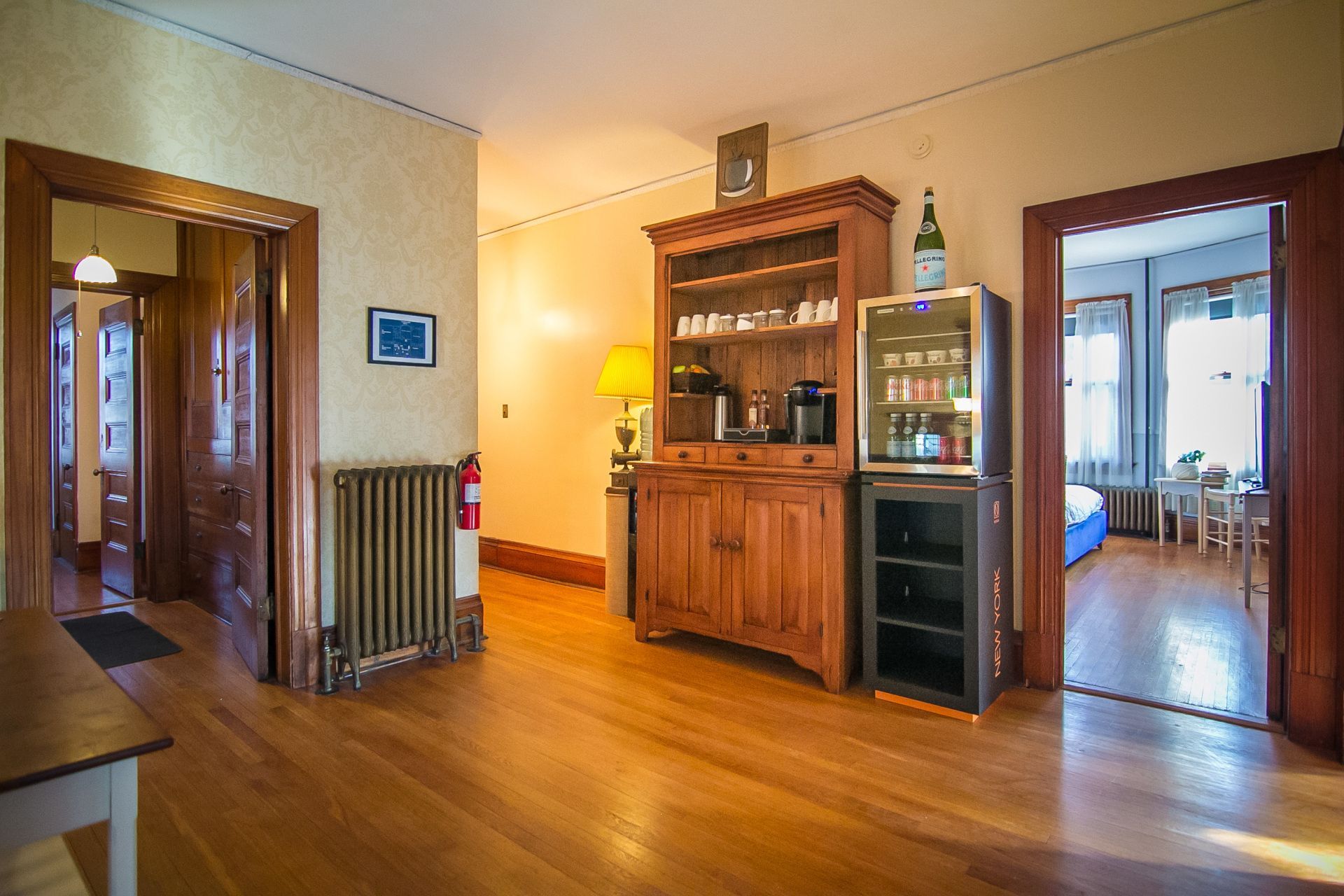 A living room with hardwood floors , a hutch , a refrigerator , a table and a refrigerator.
