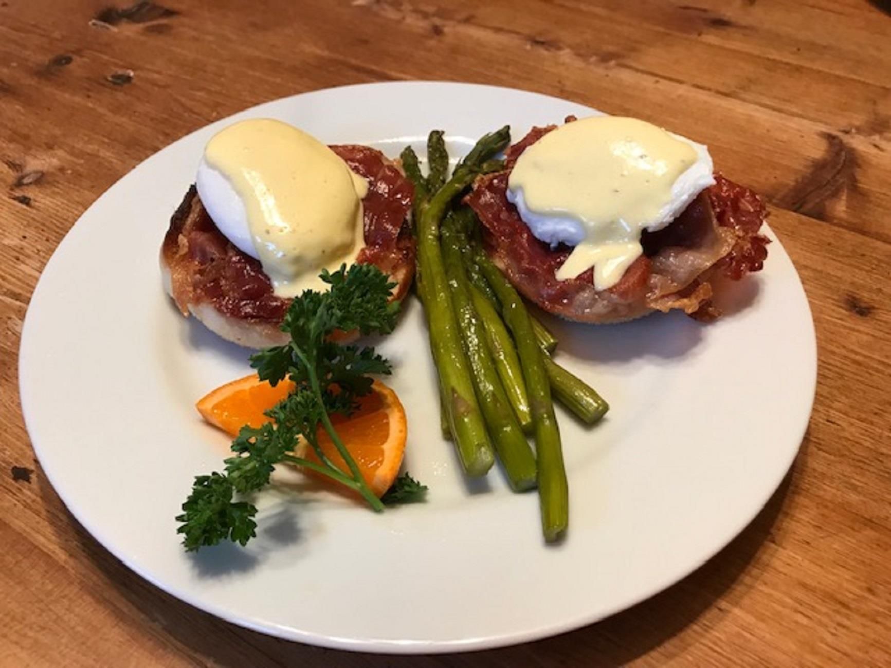 A white plate topped with eggs benedict and asparagus on a wooden table.