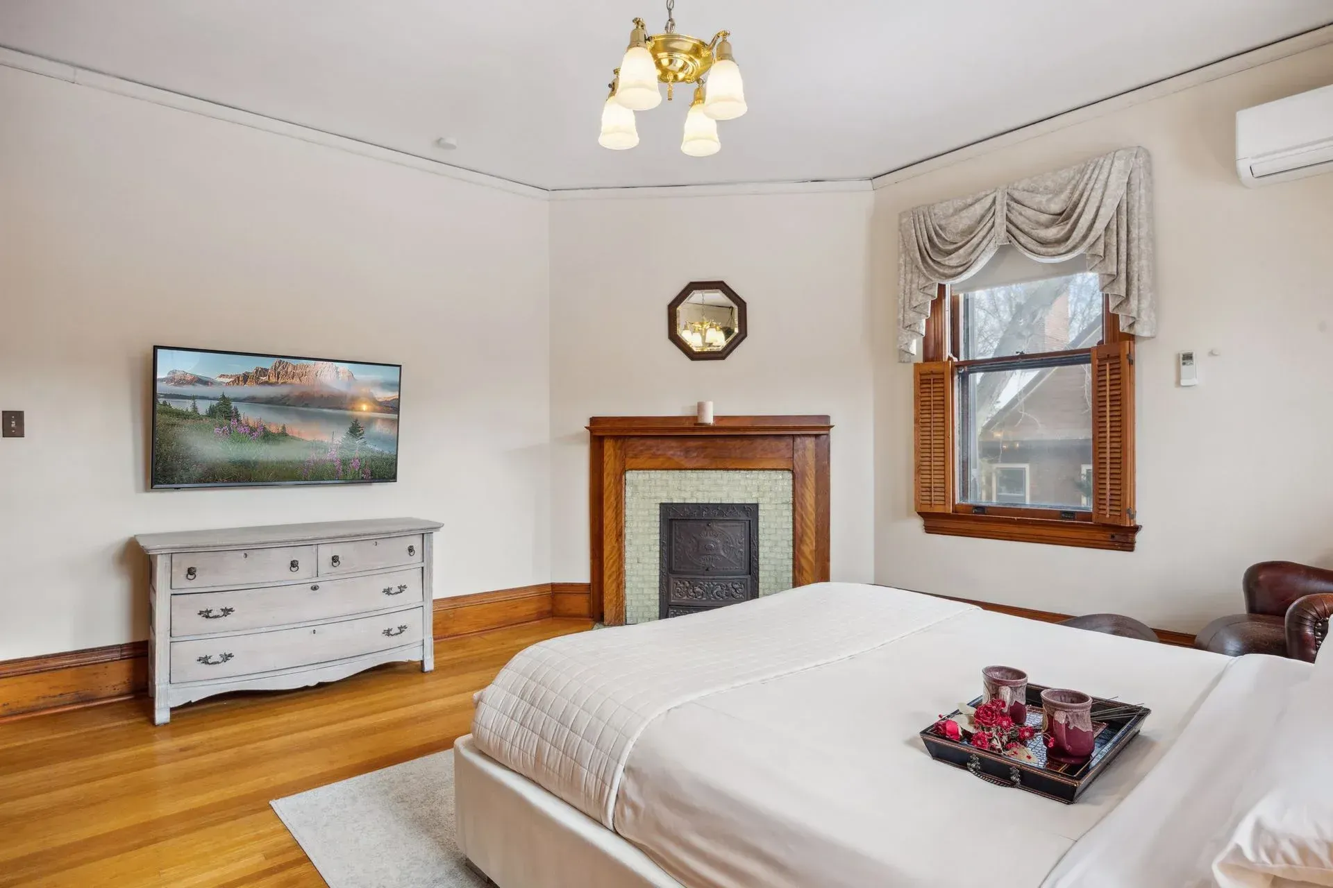 A bedroom with a bed , dresser , television and fireplace.