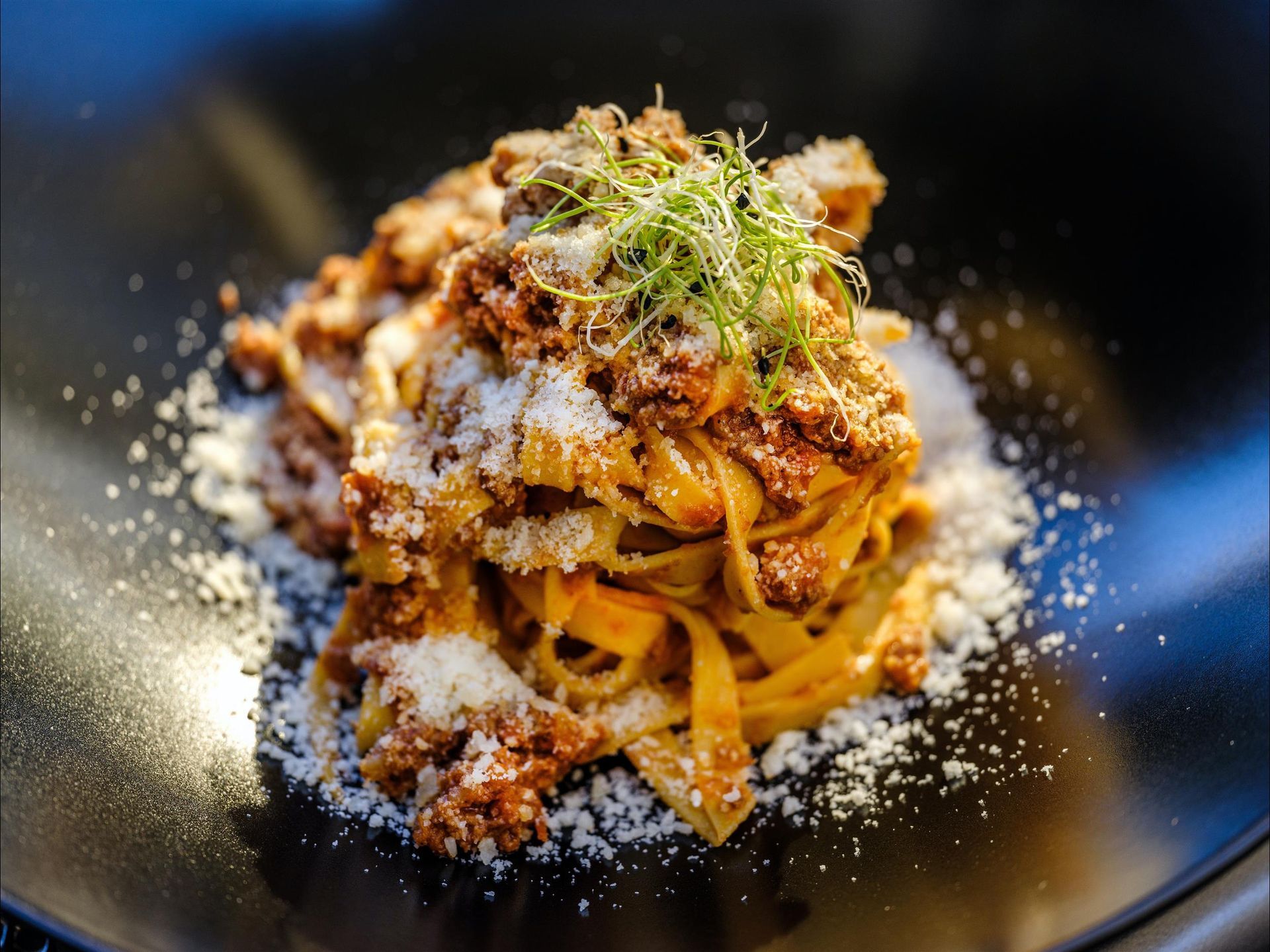 A close up of a plate of pasta with meat and cheese on a table.