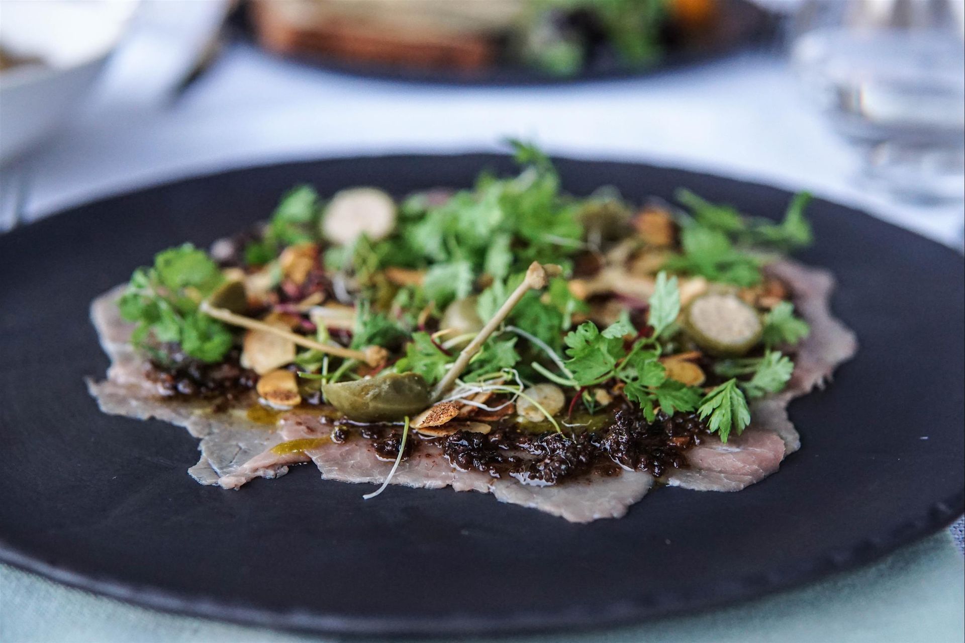 A black plate topped with meat and vegetables on a table.