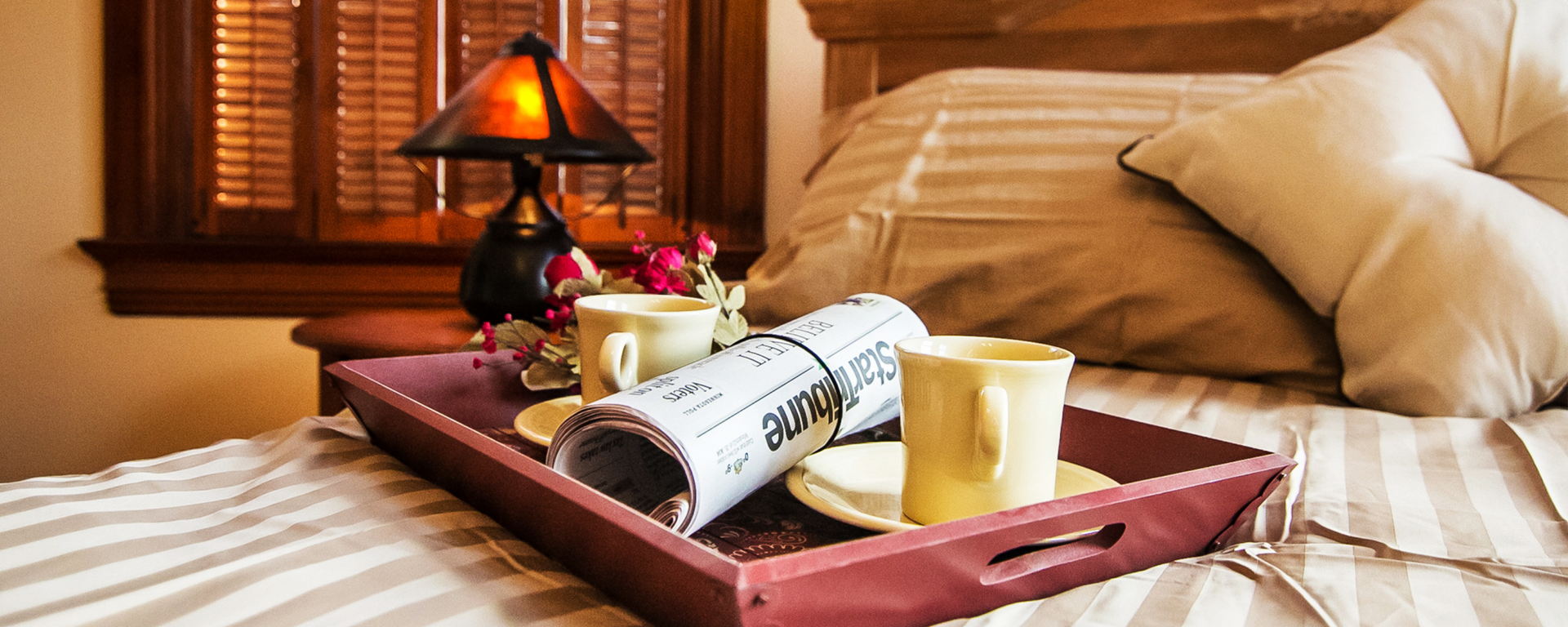 A tray with two cups of coffee and a newspaper on a bed.
