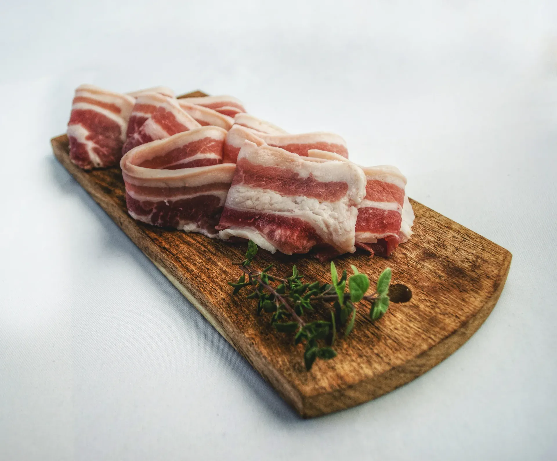 A wooden cutting board topped with slices of bacon and herbs.