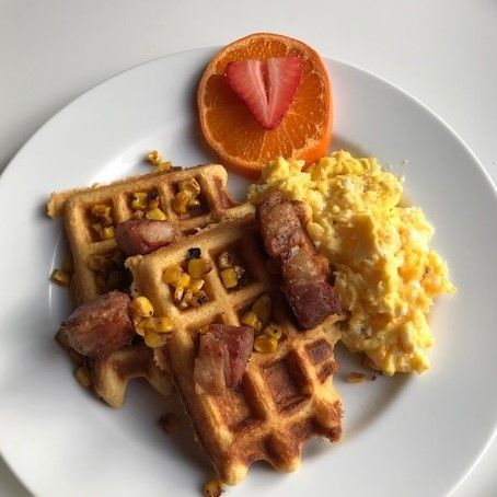 A white plate topped with waffles scrambled eggs and bacon
