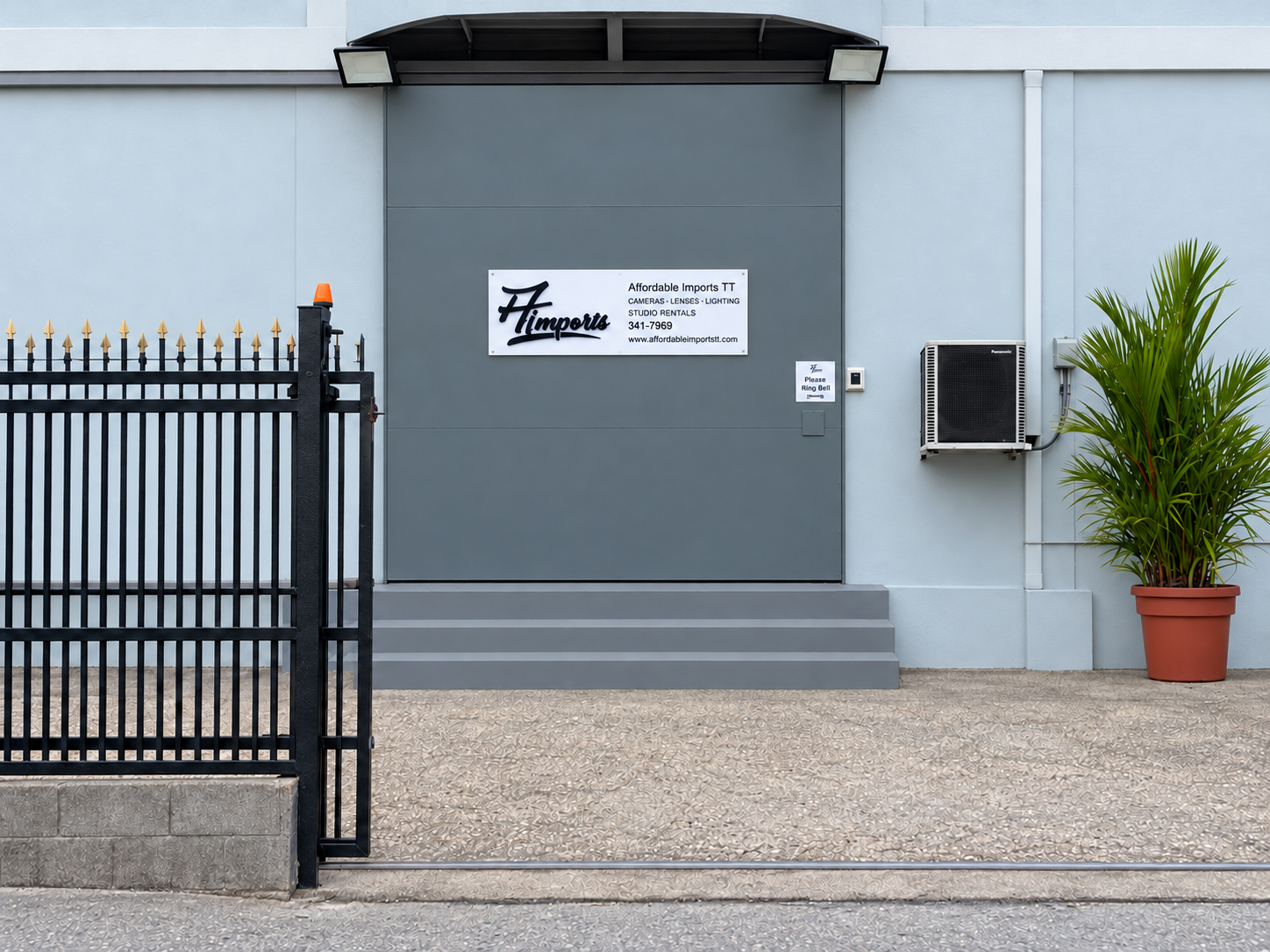 Affordable Imports TT ground-floor entrance with its sign, black gate and potted palm