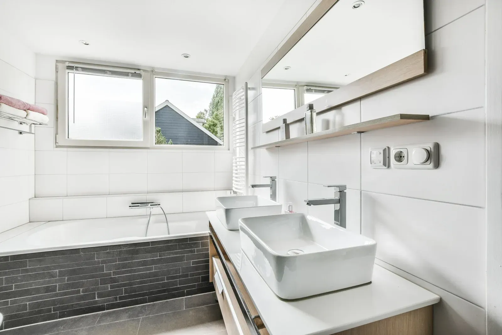 Modern bathroom with a bathtub, sinks, large mirror, and window.