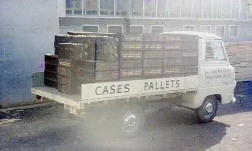 A white truck filled with cases and pallets is parked in front of a building.