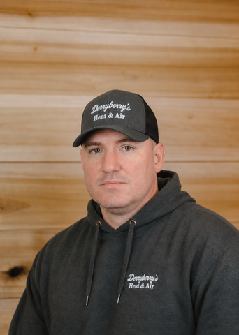 Man wearing a gray beanie and hooded sweatshirt against a wood-paneled wall, looking at the camera.