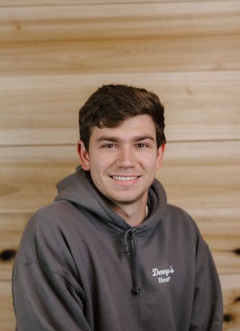 Man smiling, wearing a gray hooded sweatshirt, standing in front of a wood panel background.