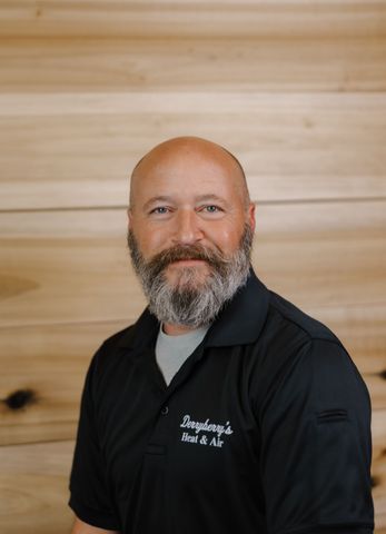 Man with a beard in a black polo shirt, standing in front of wood paneling. 