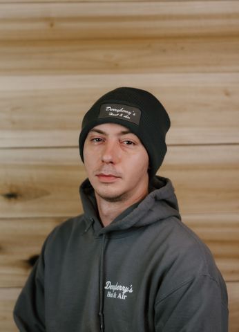 Man in gray hoodie and beanie, looking at the camera. Wooden background.