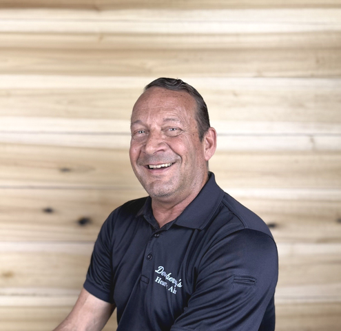 Man in black polo smiling in front of a wood-paneled wall.