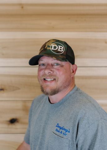 Man with a long beard and a hat wearing a gray hoodie in front of a wood panel background.