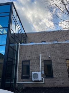Exterior view of a brick building with a glass tower on the left; a wall-mounted AC unit is visible.