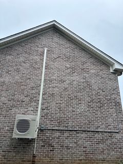 Brick house exterior with a white air conditioning unit and piping. Cloudy sky.