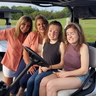 A group of women are sitting in a golf cart.