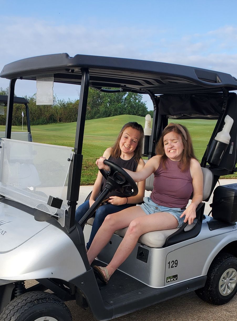 Two girls are sitting in a golf cart on a golf course.