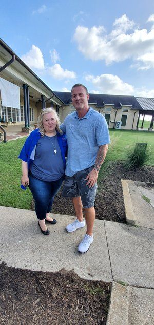 A man and a woman are standing next to each other on a sidewalk in front of a building.