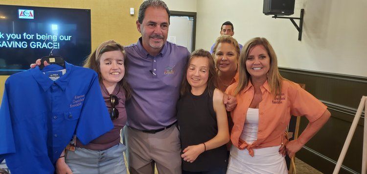 A group of people posing for a picture with a man holding a blue shirt.