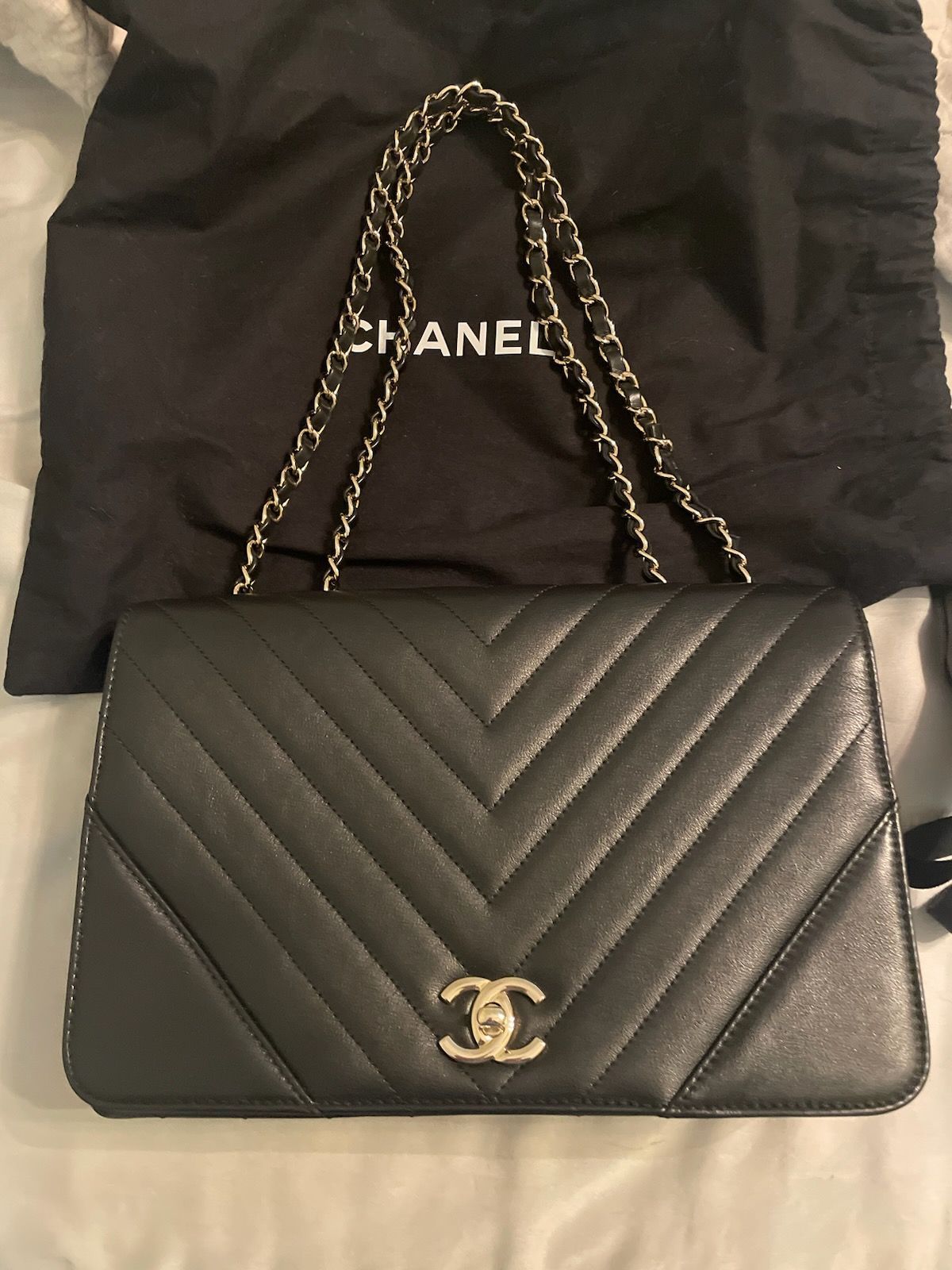 A black chanel purse is sitting on a bed next to a black bag.