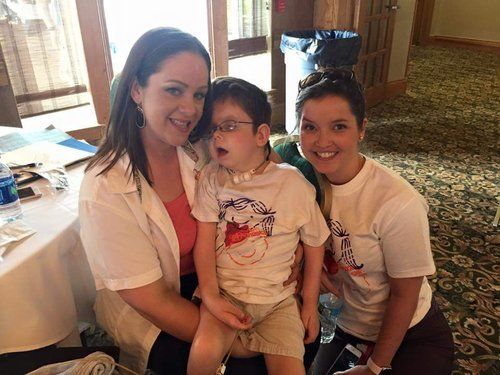 Two women are sitting next to a young boy with a necklace around his neck.