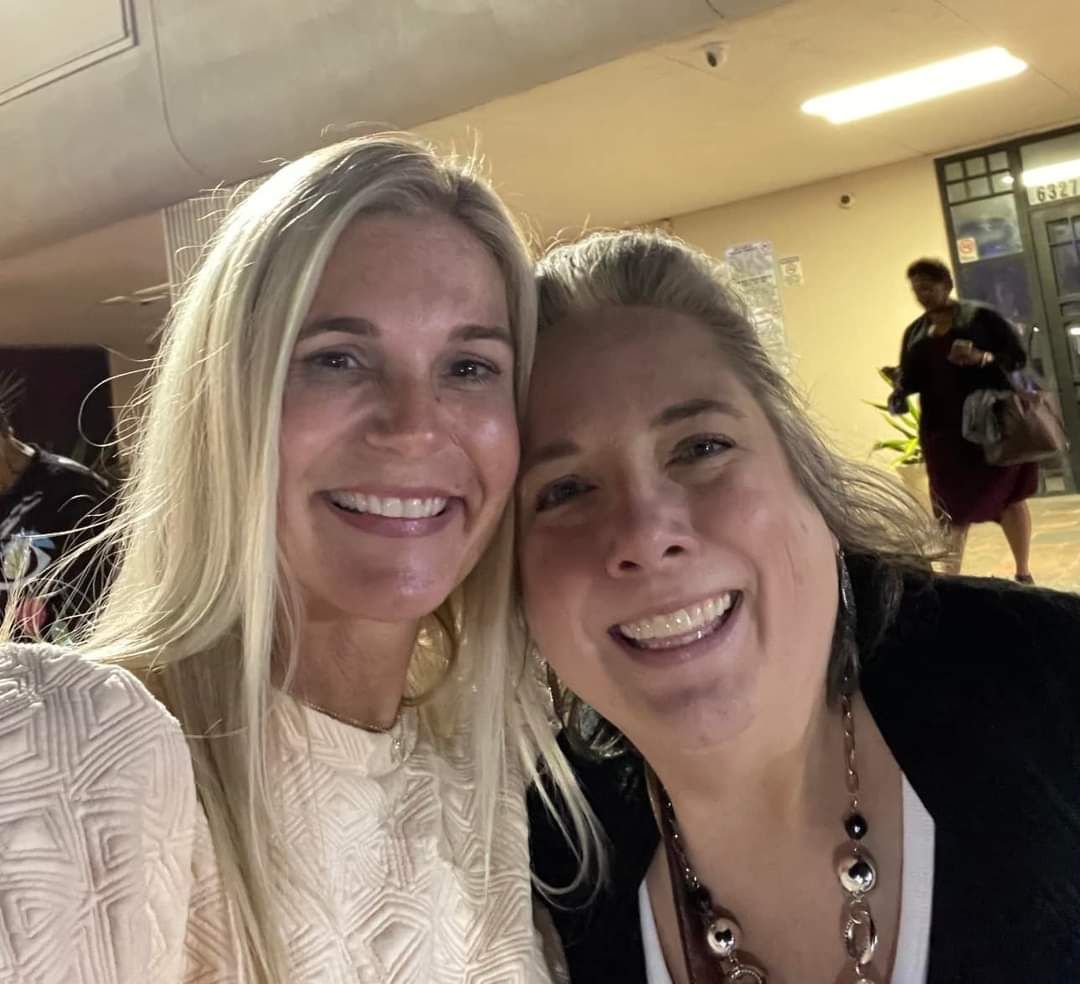 Two women are posing for a picture together and smiling for the camera.