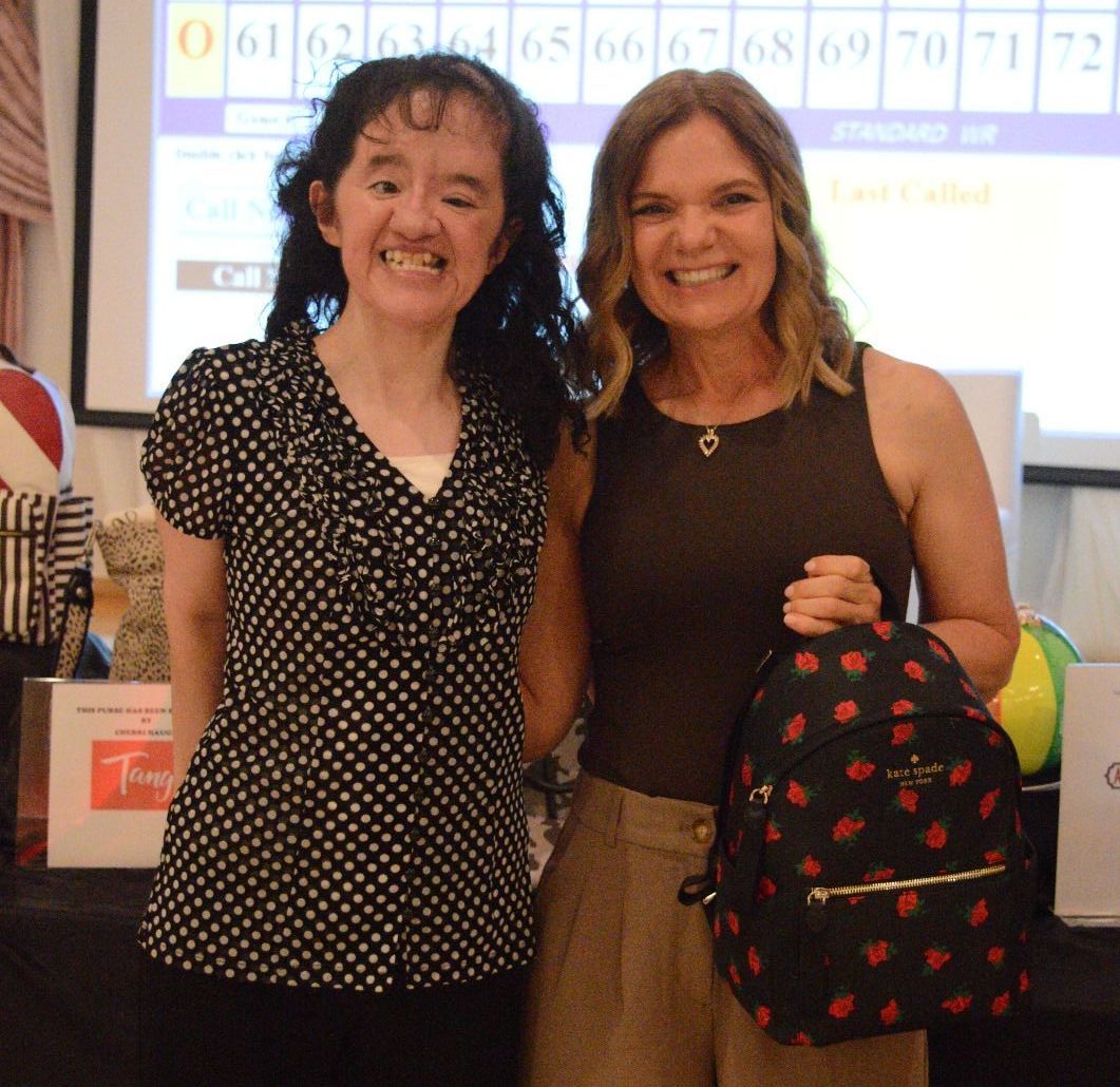 Two women are posing for a picture and one is holding a backpack
