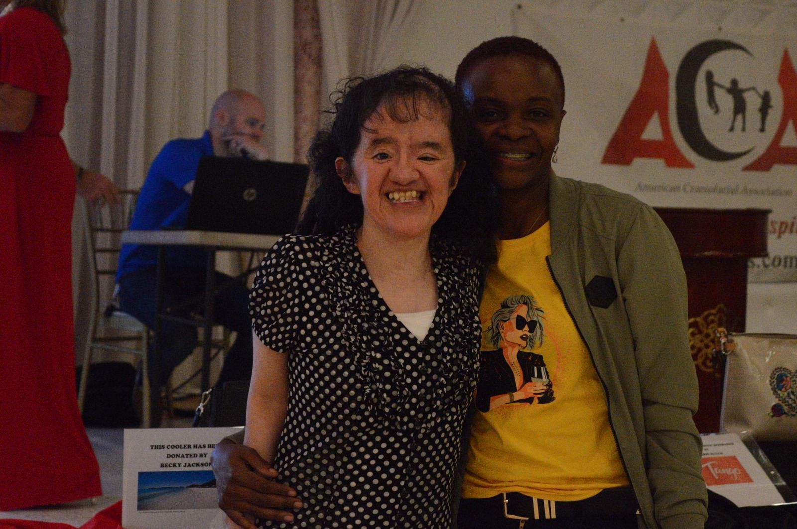 Two women posing for a picture in front of a sign that says aca