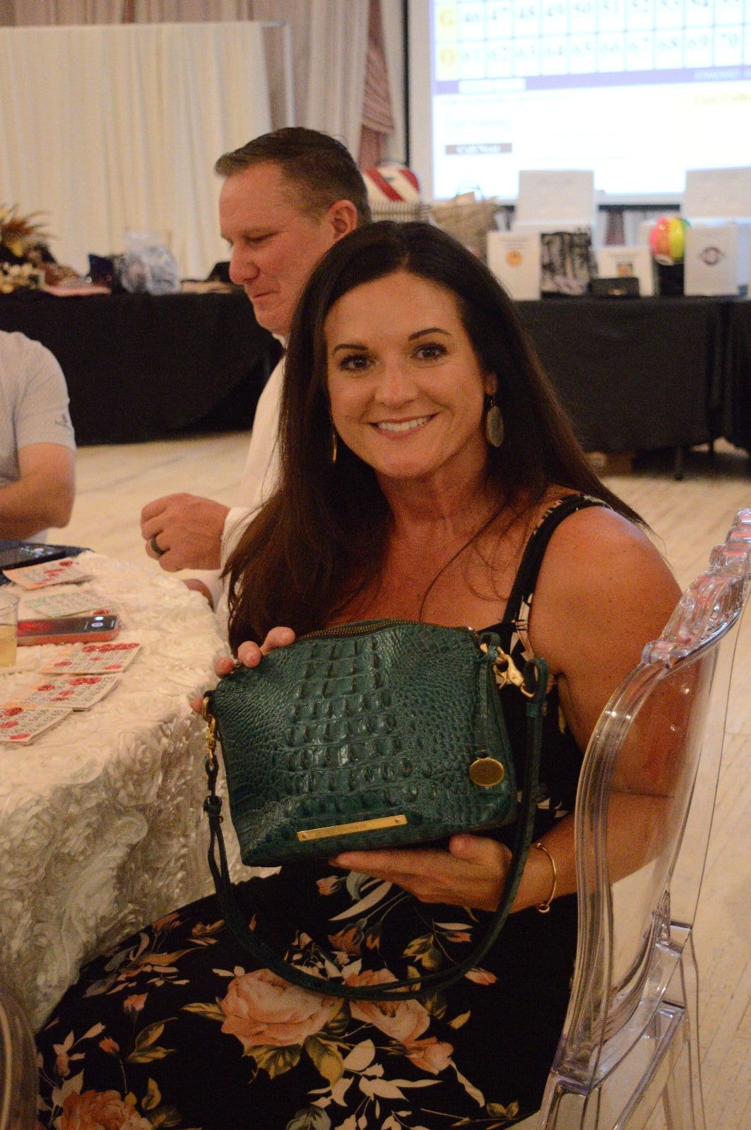 A woman is sitting in a clear chair holding a green purse.