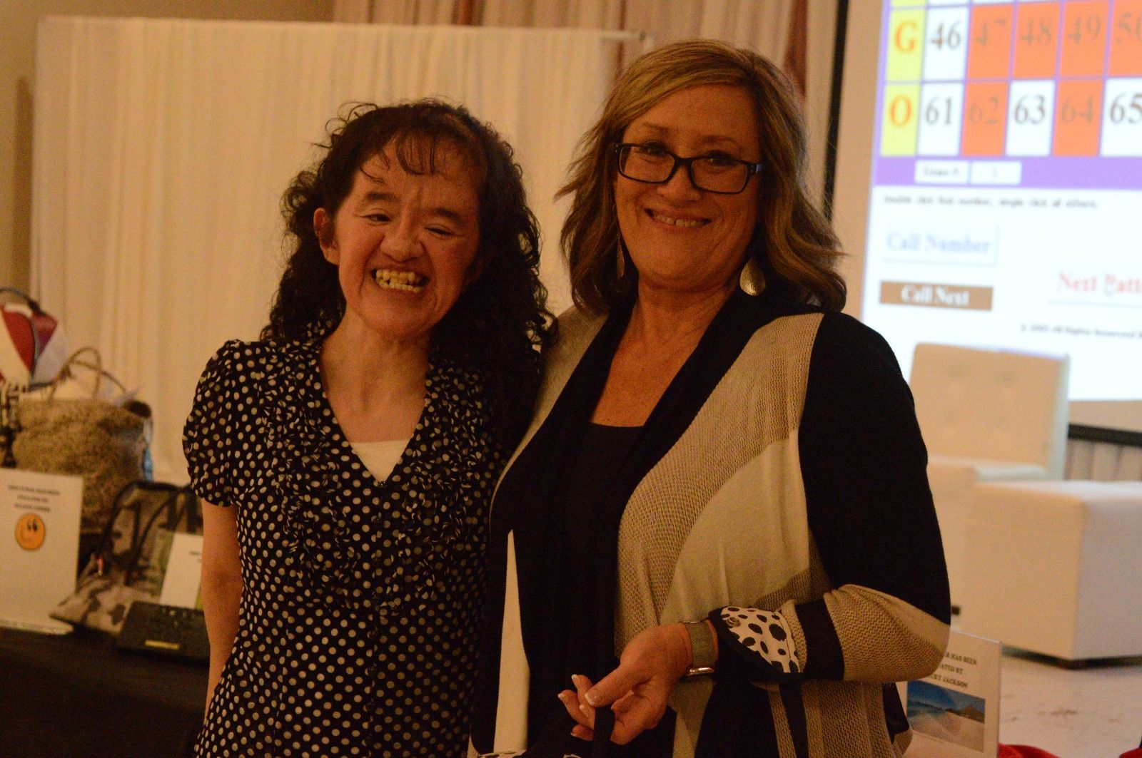 Two women are posing for a picture in front of a projector screen with numbers on it