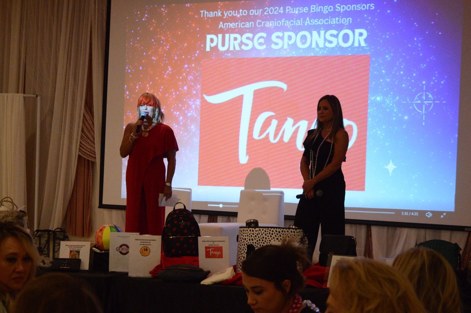 Two women are standing in front of a screen that says purse sponsor