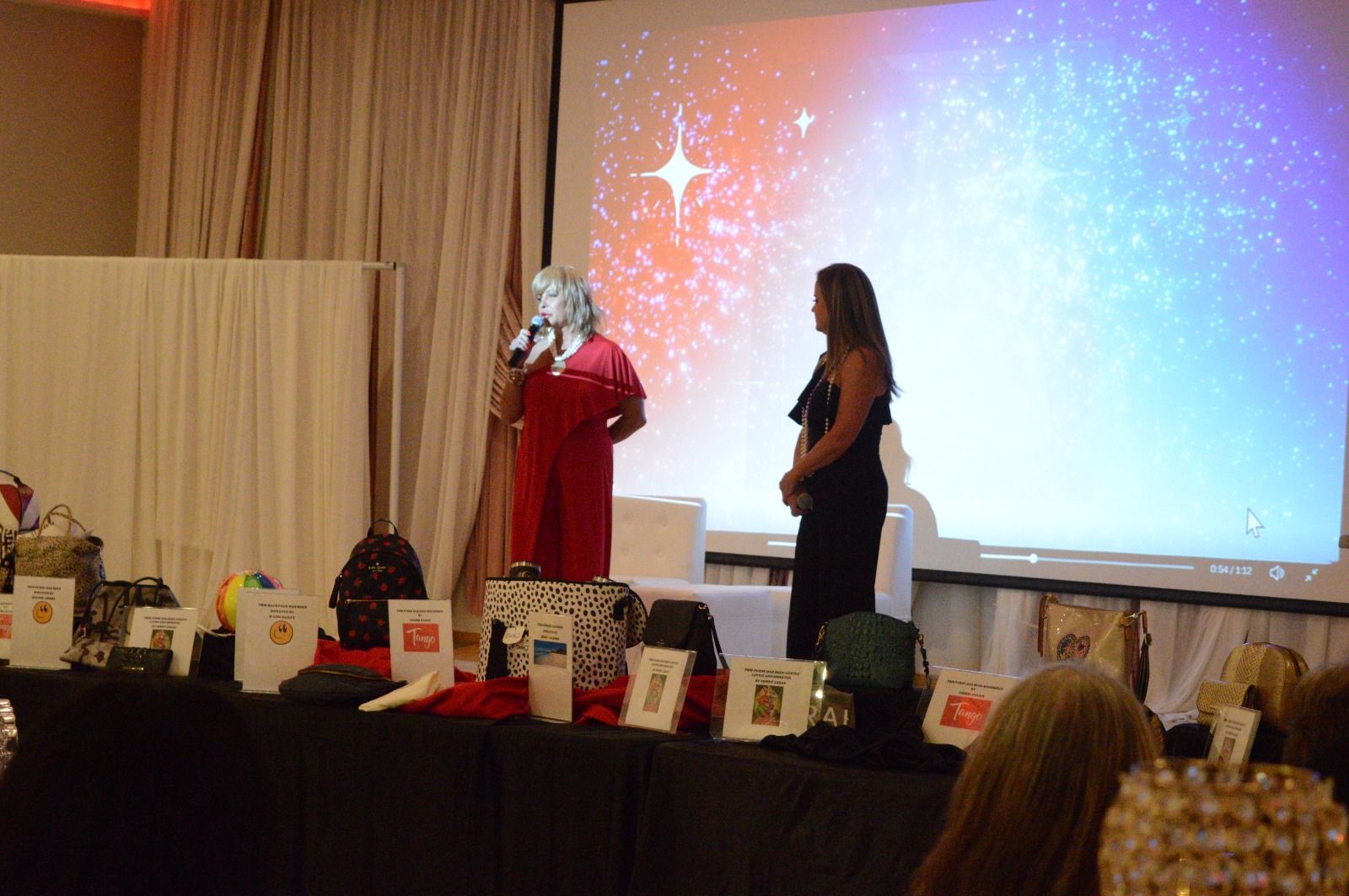 Two women are standing on a stage talking into microphones.