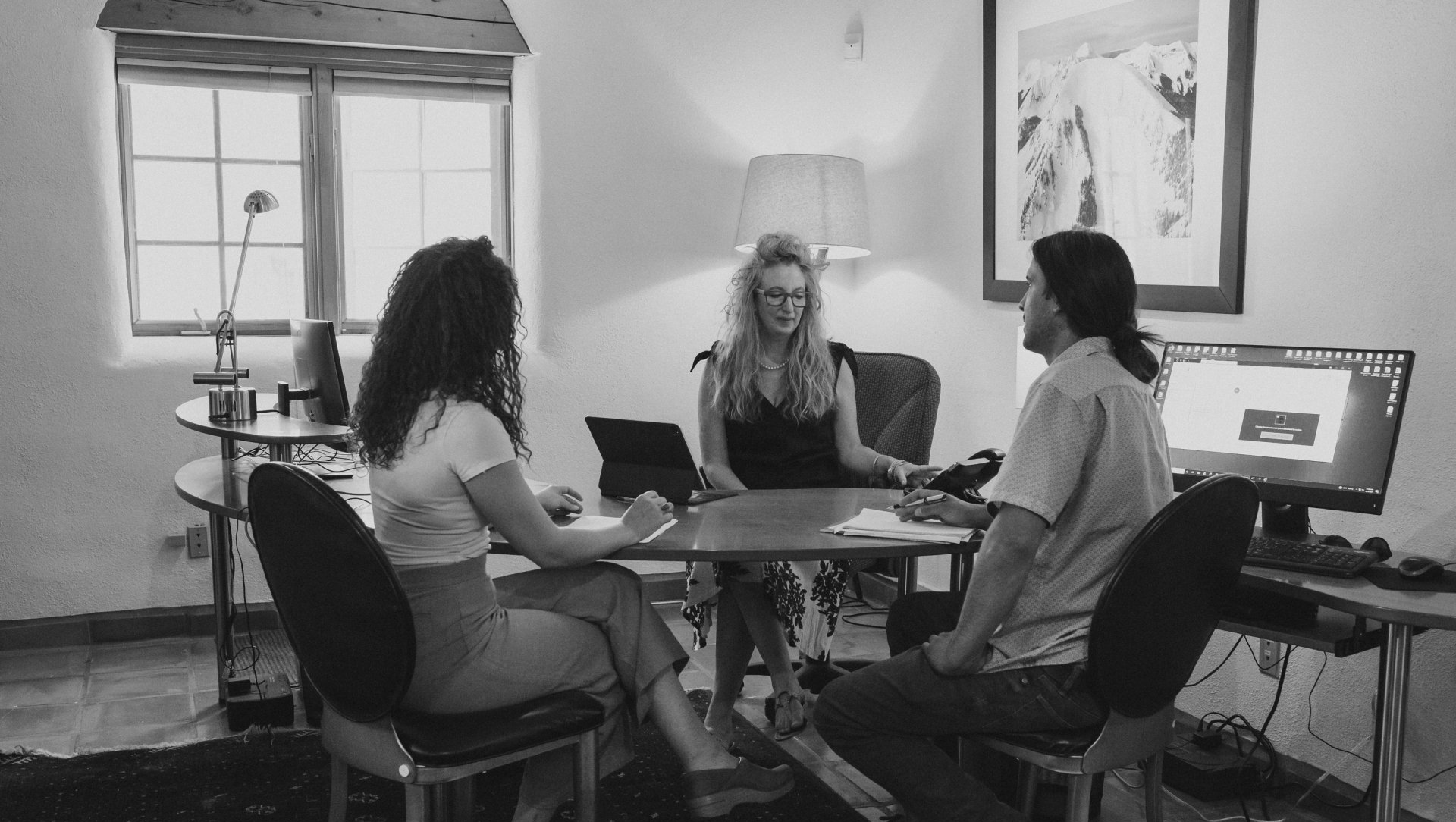 woman sitting at a large desk in an office with two of her team