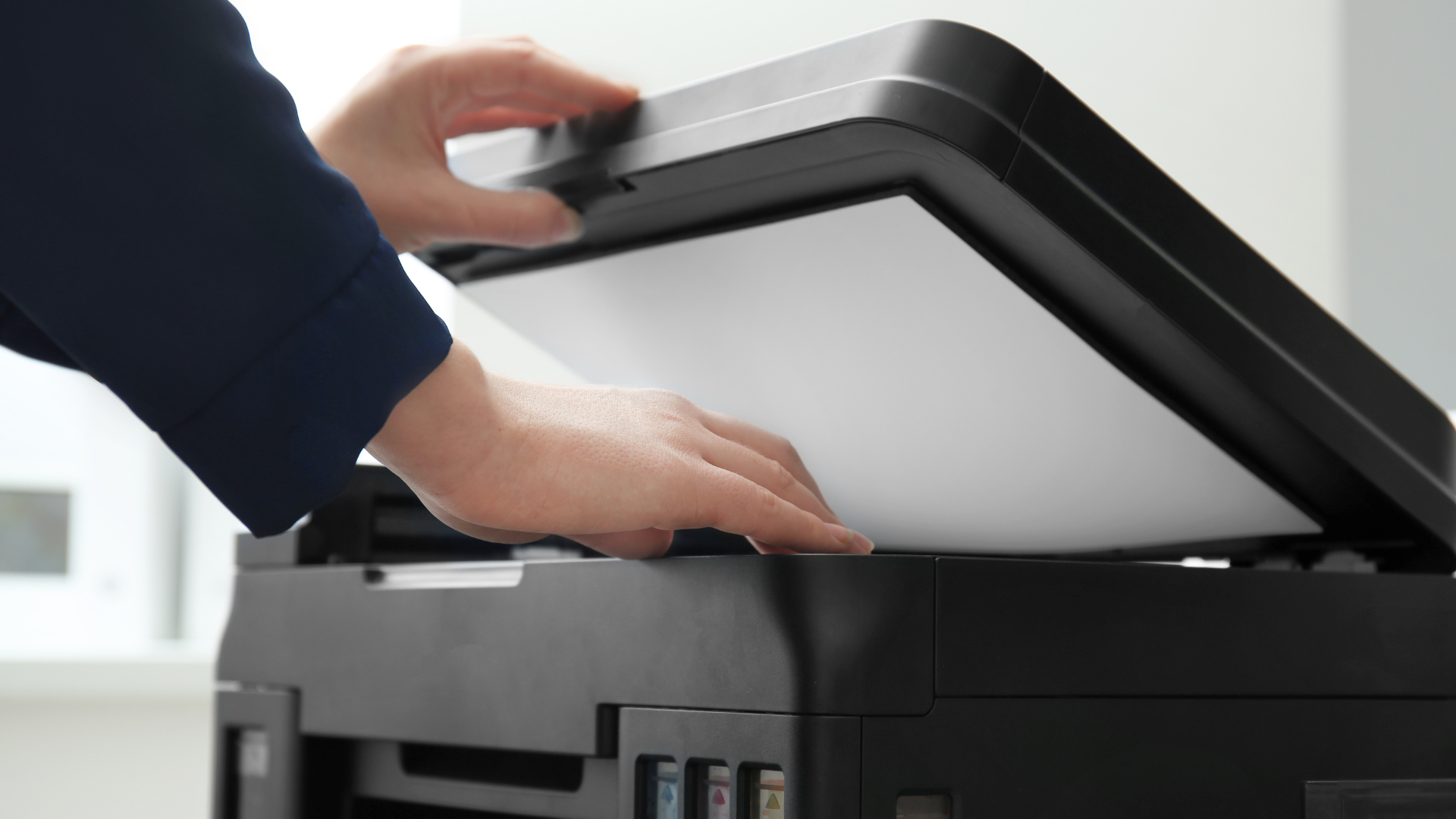 Person placing a white sheet of paper on a black scanner.