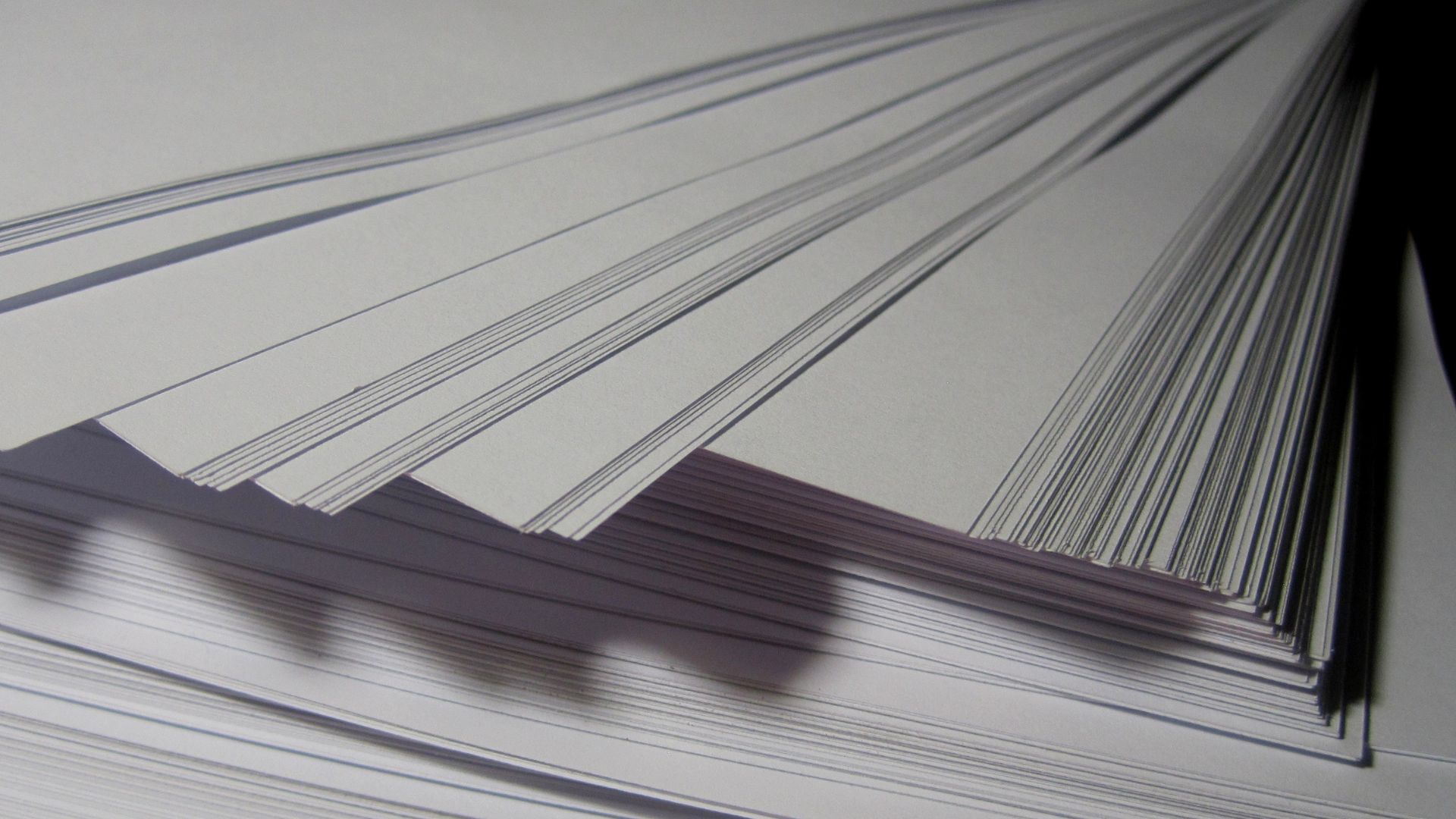 Stack of perforated, gray-striped white paper, fanned out, creating shadows.