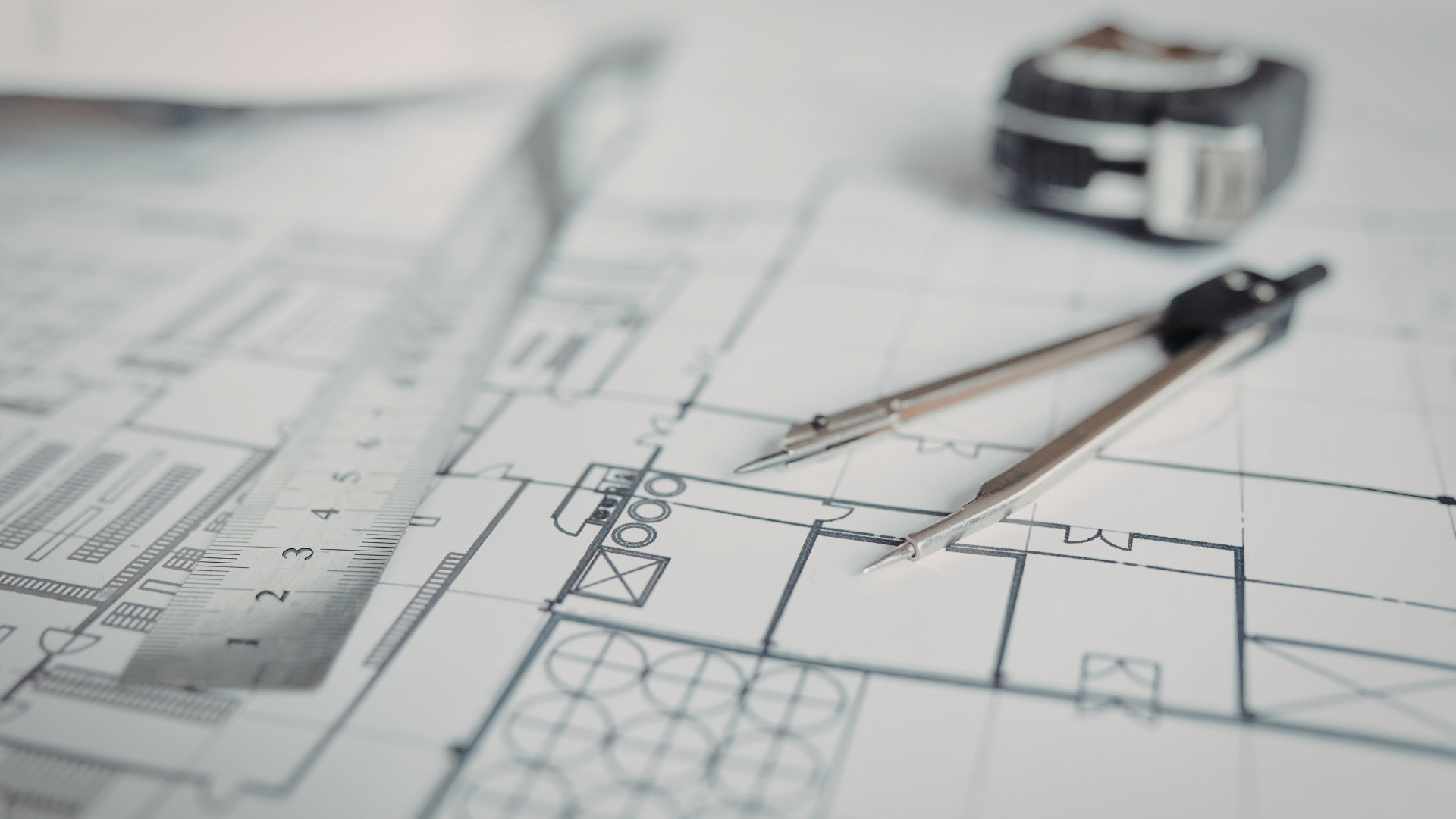 Architectural blueprints with a compass, ruler, and measuring tape.