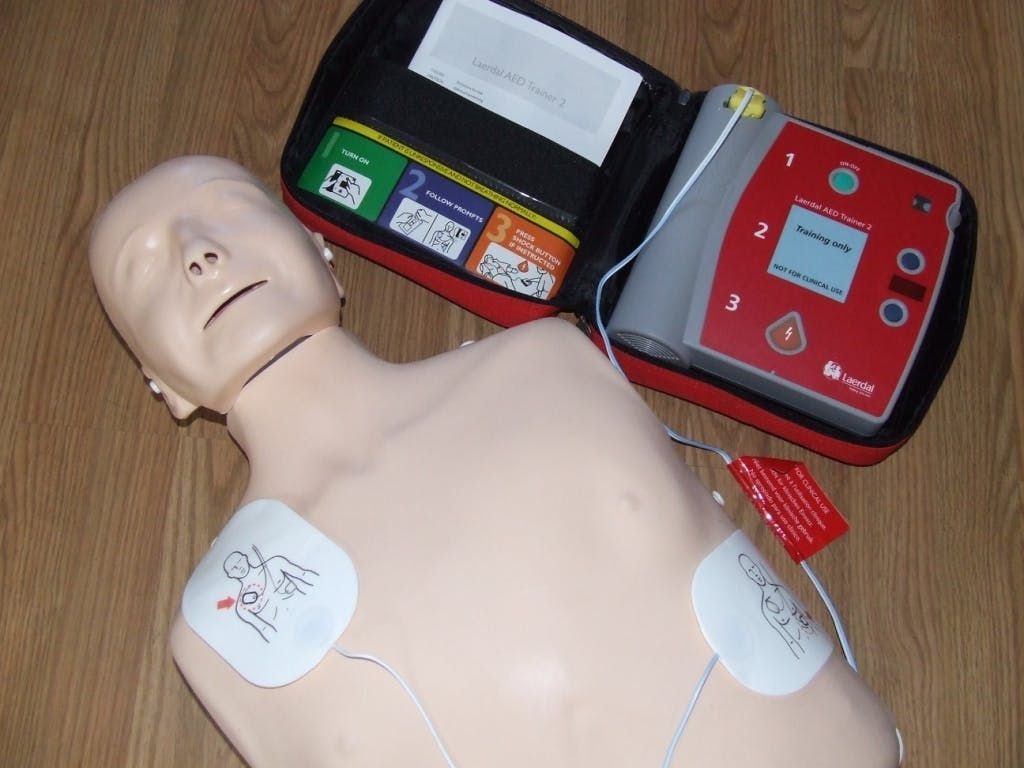 CPR training mannequin with AED pads and a red defibrillator on a wooden floor