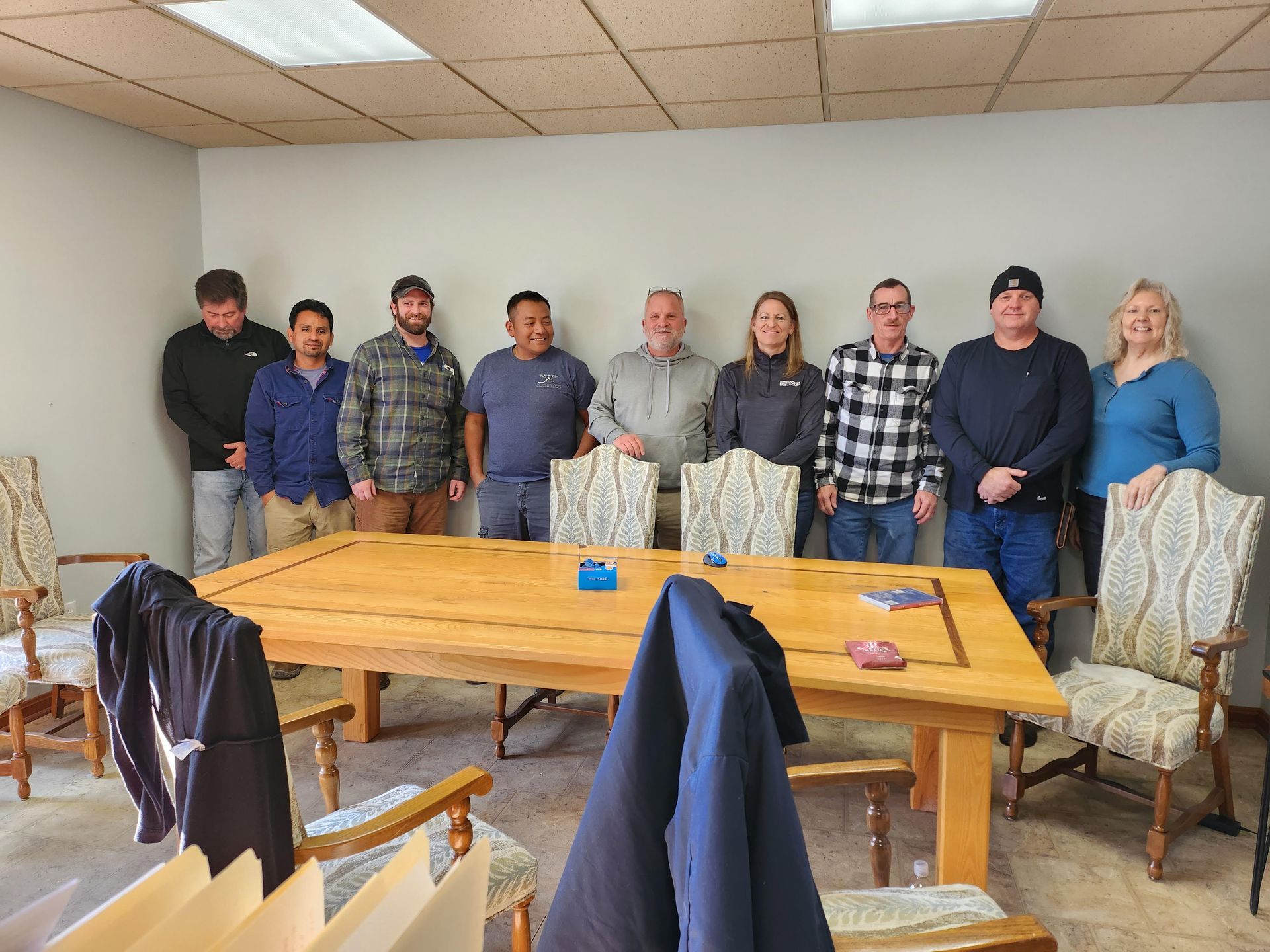 Group of people standing behind a wooden table in a meeting room with chairs and jackets in the foreground