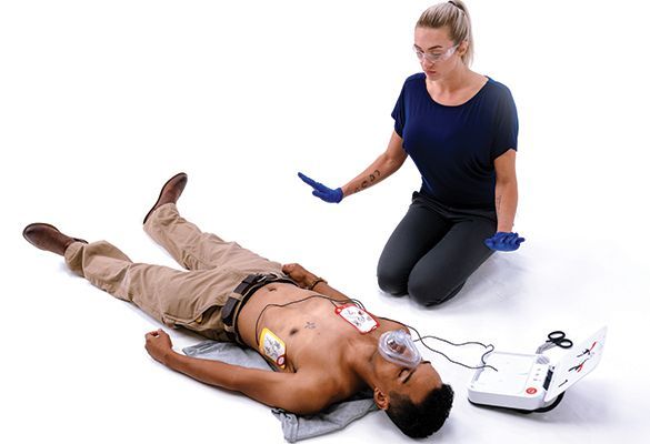 Training manikin with AED pads, oxygen mask, and responder kneeling beside it