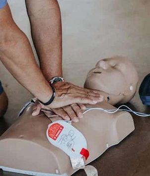 Hands performing CPR chest compressions on a training manikin with AED pads attached.