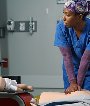 Nurse in blue scrubs performing CPR on a patient mannequin in a training room