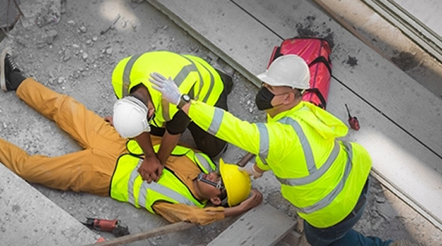 Construction workers in neon vests and hard hats helping an injured person on a concrete slope