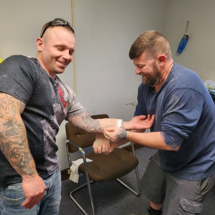Two men in a room wrapping a wrist with a bandage, one smiling