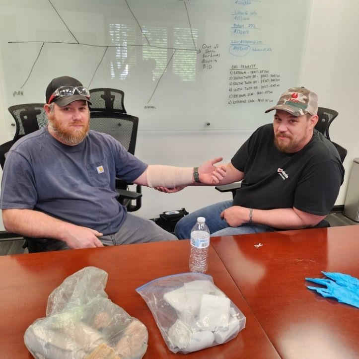 Two men seated at a conference table, reaching hands across it in an office setting.