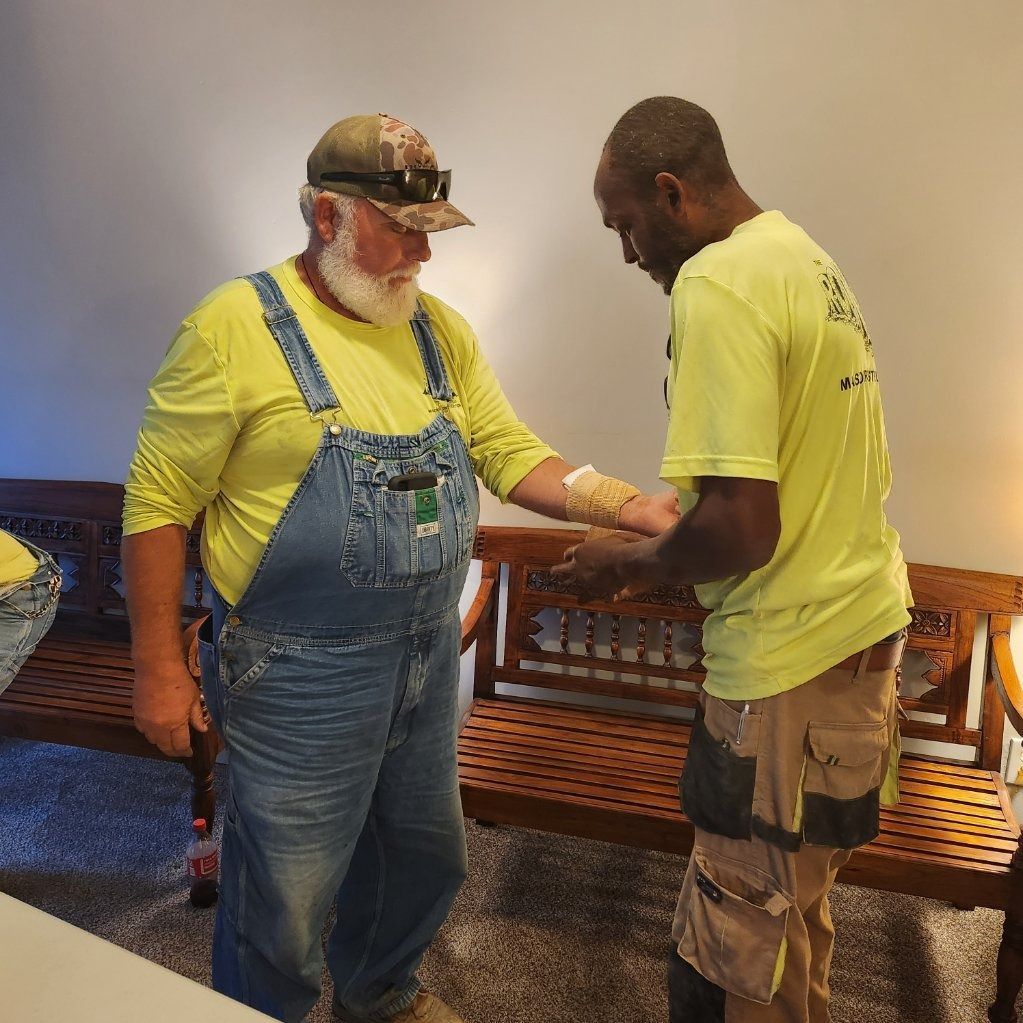 Two men in yellow shirts shake hands indoors beside a wooden bench.