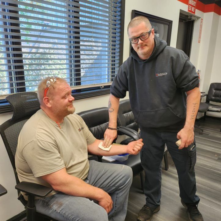 Two men in an office; one is seated while the other measures his forearm.