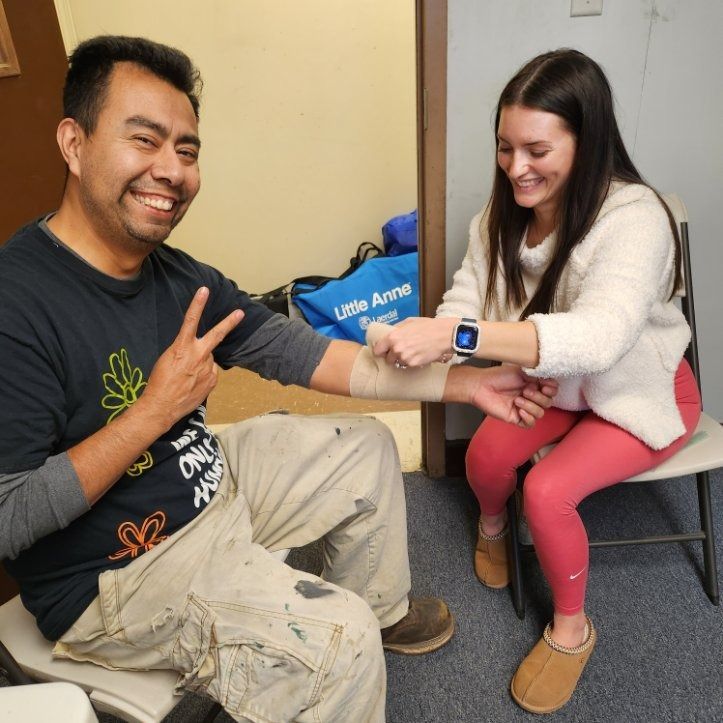 Two people smiling during a seated arm blood pressure check in a clinic room